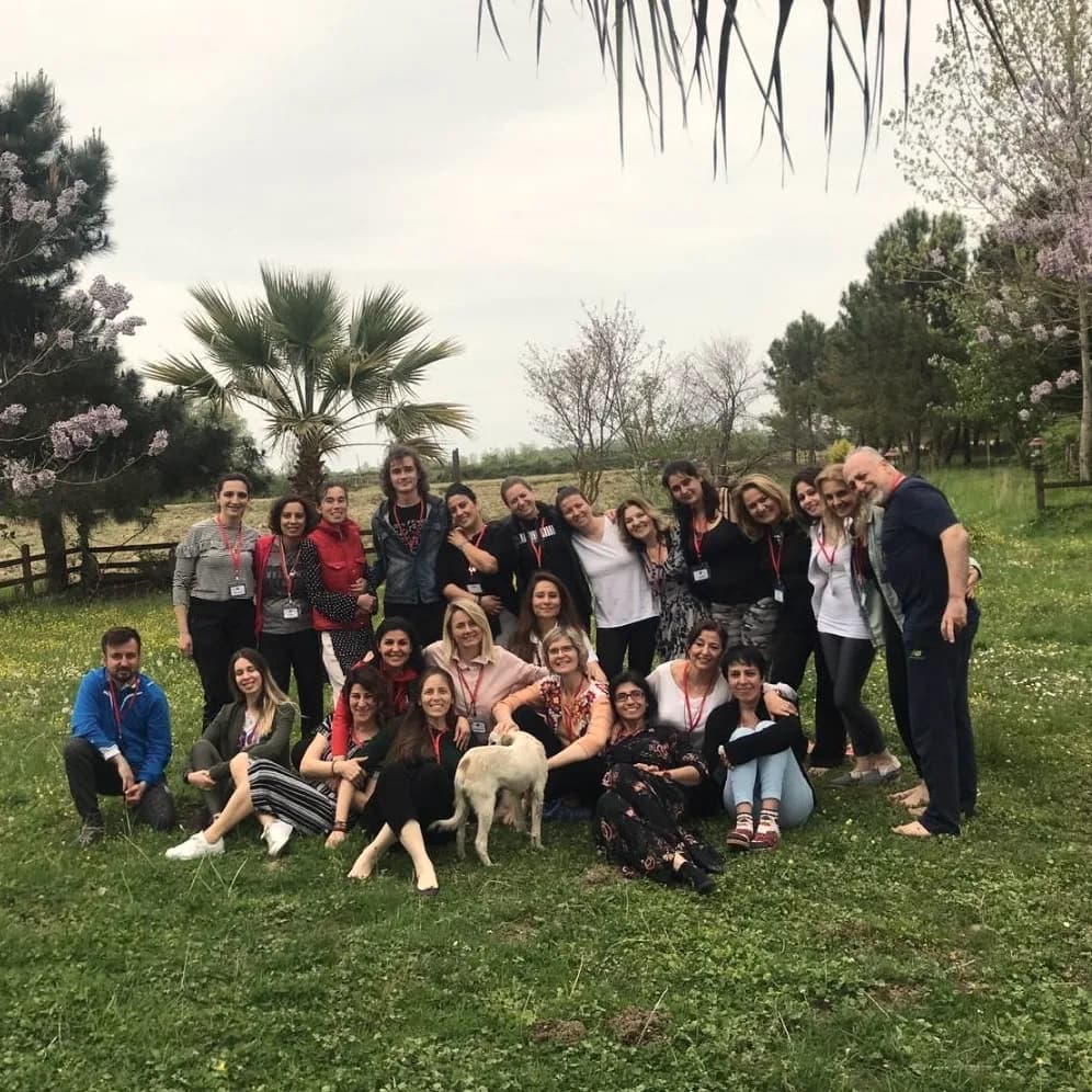 Palmiyeli bir bahçede çimenlerin üzerinde toplu fotoğraf veren gülümseyen bir grup